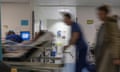 A blurred image of a hospital worker pushing a person on a bed along a corridor