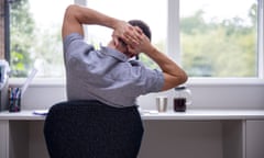 Posed by model Rear View Of Man Working From Home On Computer In Home Office Stretching At Desk