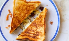 Top view of a cheese toastie, cut into two triangles with a delightful cheese pull, on a white plate with a blue rim.