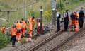 Workers in orange hi-vis clothing and gendarmes gathered at the edge of a railway line