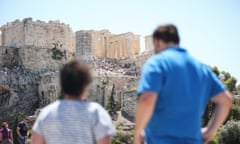 Tourists look up at the ancient Temple of the Parthenon on the Acropolis hill in Athens