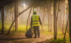 A man in a hi-vis vest seen from behind as he picks rubbish amid some trees