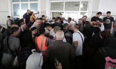 A crowd of people holding passports wait to pass through a door