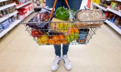 a shopper carries a basket of everyday grocery items, including fresh fruit, bread, and tinned food