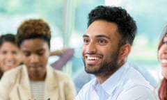 Smiling business professional attends finance conference<br>Handsome businessman smiles while listening to lecture during business conference. His colleagues are sitting beside him.