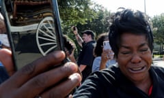 A woman cries while holding a smartphone up. In the reflection of the phone's case, a white carriage can be seen.