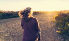 Rear view of woman walking on dirt road during sunset