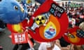 Protesters sit in the road holding whale balloons and signs with nuclear and flame symbols and images of fish and whales