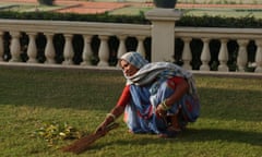 A cleaner in Jaipur, India, squats to sweep leaves from a lawn.