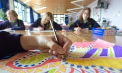 Closeup of a school pupil's hand drawing a colourful picture, while 3 other female students sit working in the background