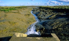 Foamy water flowing from a sewage outflow across mucky terrain