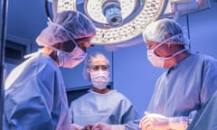 Doctors wearing surgical masks and gowns performing an operation on patient in hospital operating theatre