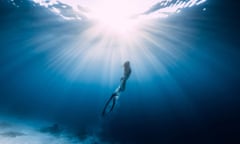 Woman freediver glides over sandy seabed with fins