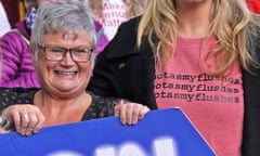The MP Carolyn Harris at a protest against ongoing prescription charges for HRT – she is smiling widely and holding a large placard, and standing next to a woman with a T-shirt reading 'hot as my flushes'