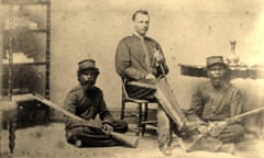 A black-and-white photo of a seated young man in police uniform holding a ceremonial sword while two Aboriginal troopers sit on the ground on either side of him