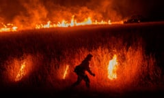 Silhouette of a person walking in front of tall grass on fire.