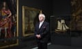 David Starkey stands with clasped hands at an exhibition including paintings and a model ship