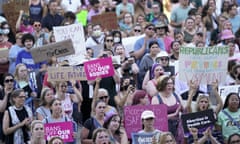 A sea of mostly women wearing summer clothes holding signs that are mostly pink and white.
