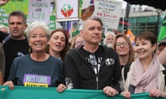 Man flanked by two women at demonstration with protesters and placards in background