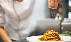 Close-up of chef in whites sprinkling a seasoning on to a plate of food