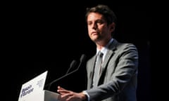 A man in a grey suit and grey tie gives a speech from a podium