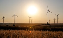 Wind turbines are seen on a wind farm on a field between agricultural produce against a sunset in a countryside in a village near Radom