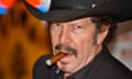 a middle-aged white na with a mustache and chin hair wearing a black cowboy hat smokes a cigar