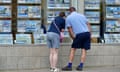 Two people, wearing shorts and T-shirts, inspect a property advert in an estate agent window in Swanage, Dorset.