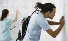 Male college student at bulletin board copying information