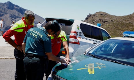 A Civil Guard officer and others study a map on the bonnet of a car