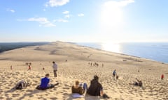 A huge sandy dune with the sun on the sea in the distance.