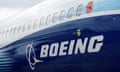 Closeup of side of jetliner with row of oval windows, with white background and dark blue below, with Boeing logo.