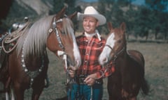 Country and western singer Gene Autry, dressed in cowboy hat and plaid shirt, poses with two horses, circa 1955