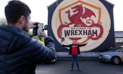 A Wrexham fan poses for a picture by the Welcome to Wrexham mural.