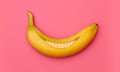 A banana cut into a smile inside its skin, against a pink background