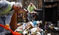 Two refuse workers in PPE clearing up a large amount of rubbish that has spilled from a public bin into the street