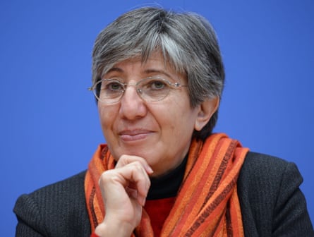 A middle-aged woman with short hair and small oval glasses looks at the camera wryly.