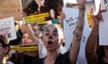 A woman with her face painted with dog features shouts at a protest as other around her hold up placards