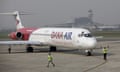 Red and white Dana Air plane on a runway with airport staff signalling