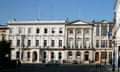 The East India Club in St James's Square, London: a large cream-painted historic building with arched windows on the ground floor and a covered doorway, balconies on the first floor and white-painted stonework. A similar building but with pillars adjoins it at the corner of the grand square.