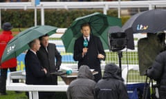 Ed Chamberlin shelters under an umbrella alongside Sir Anthony McCoy and Luke Harvey at Cheltenham