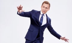 Tom Hiddleston wearing a blue suit and striking a pose with arms in the air