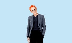 Fran Healy wearing a black top and trousers, and a grey jacket, with orange hair and black-framed glasses