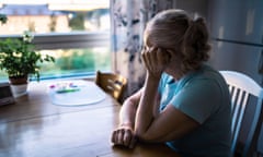 An older woman sitting at a table in her home looking  depressed