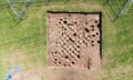 A view looking down on a sandy-coloured excavation site set in a green field