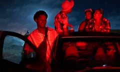 A young man gets behind the wheel of a pickup truck. There is someone in the passenger seat and three people in the truck bed.