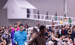 Models walking down a runway descending from a white hut