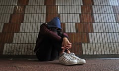 A young person wearing a hooded top and trainers sitting in an underpass
