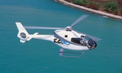 White helicopter over azure water with a coastline below.