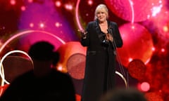 Sarah Lancashire speaking on stage against a backdrop image of abstract glittery red balloons